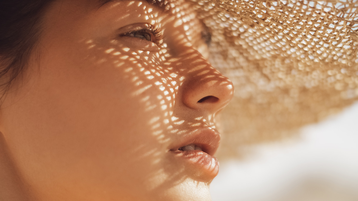 A closeup of a young woman wearing a straw hat in direct sun